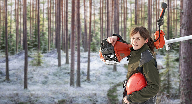 Kvinna i snötäckt skog bär en orange och vit röjsåg på axeln